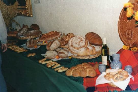 Festtafel mit verschiedenen Broten, Weinkrug und Tongeschirr auf roter Decke